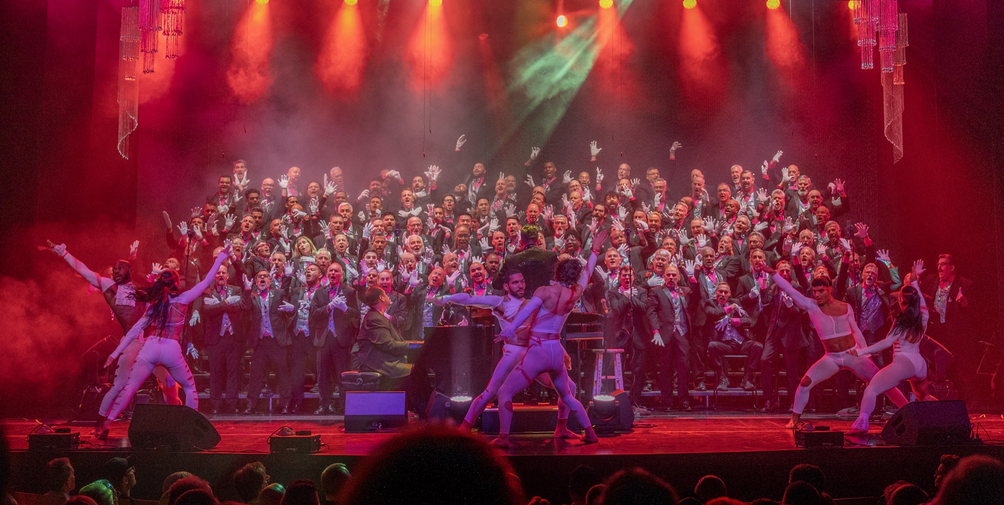 GMCSF chorus performing on stage with dancers under red concert lighting.