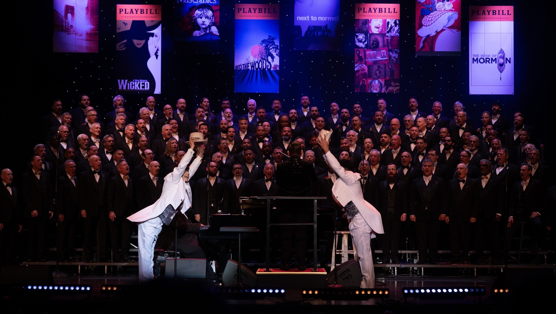 GMCSF chorus performing Broadway music on stage with playbill banners above them.